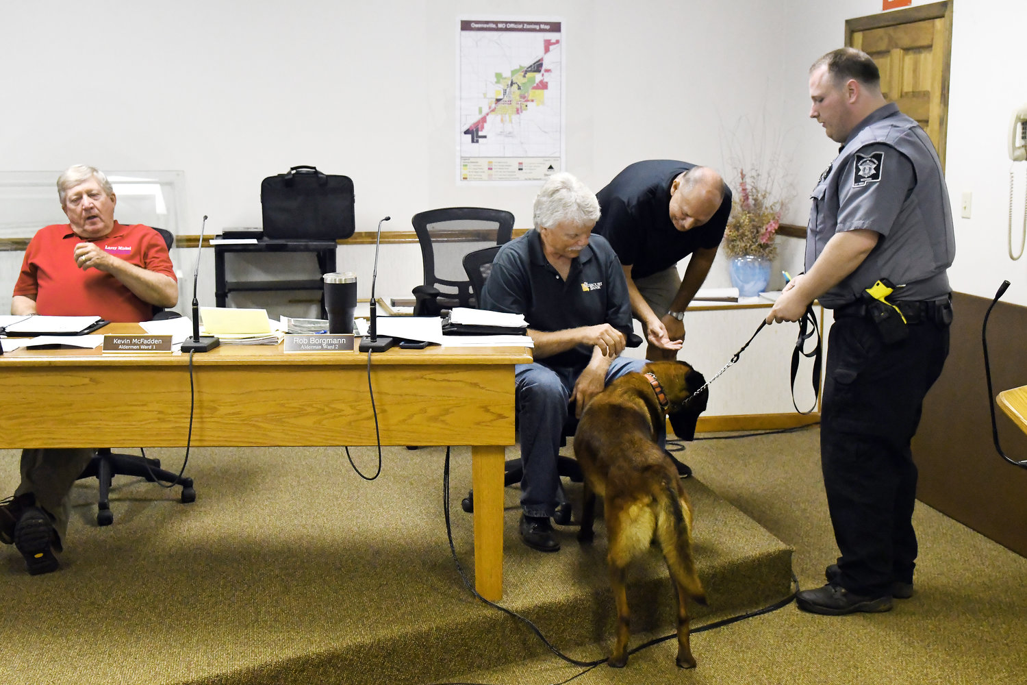 COMMISSION MEMBERS Jim Holland (seated) and Jerry Lairmore greet the sheriff’s patrol’s newest addition, K-9 unit “Raffa” and the dog’s handler, Deputy Joe Lynch. Presiding Commissioner Larry Miskel is seated on the left. Brian Dowdy, a retired lawman operating “Dogs on Duty” in Troy, Mo., trains and donates police K-9s.